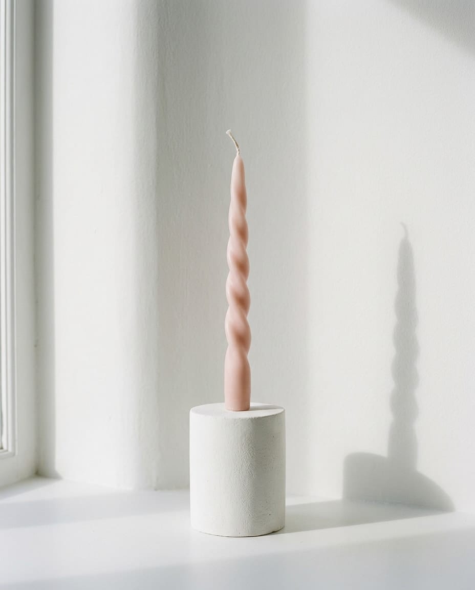 A pale pink twisted candle standing on a white surface